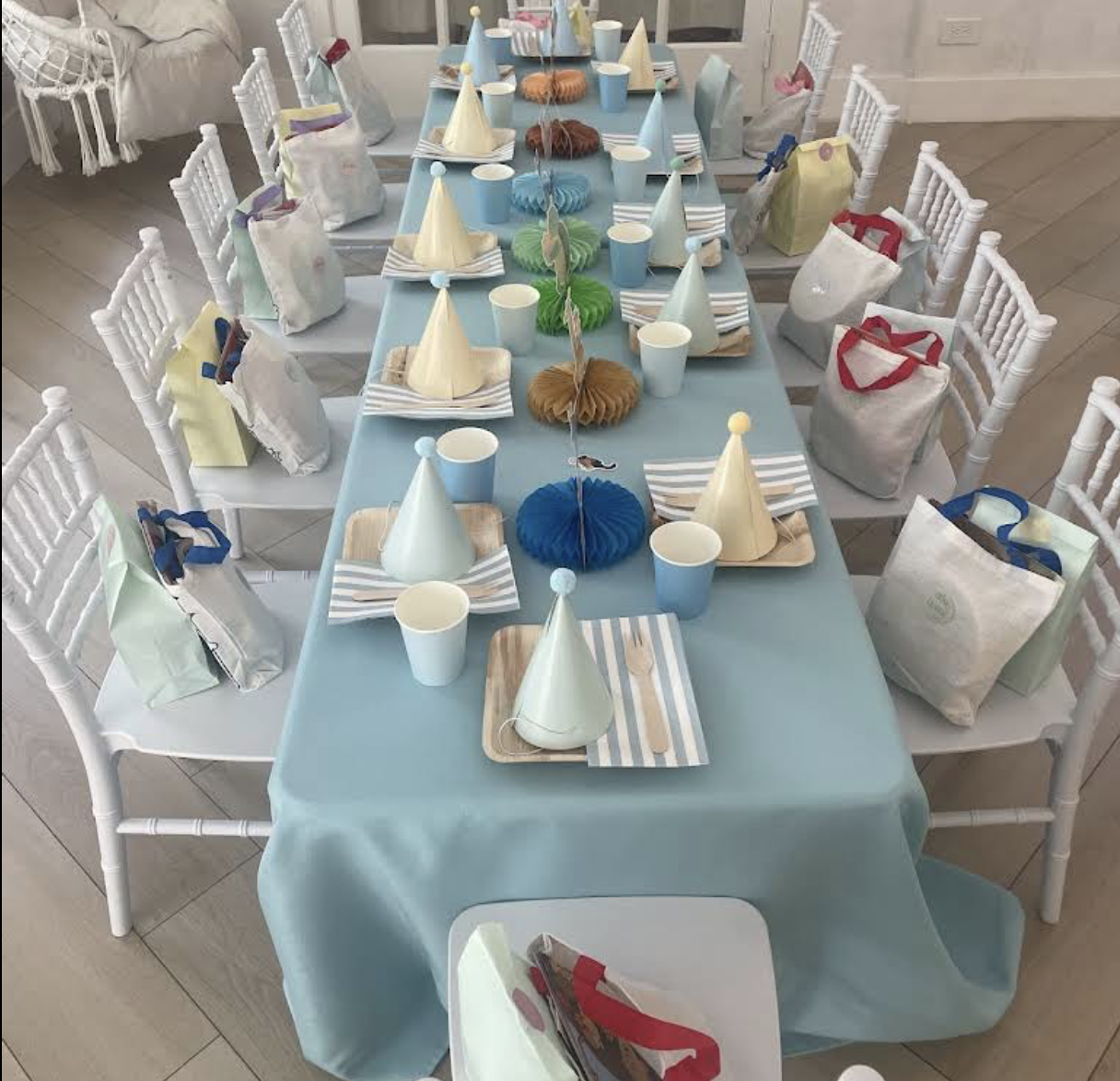 Blue birthday table with party hats, favor bags and honeycomb centerpieces