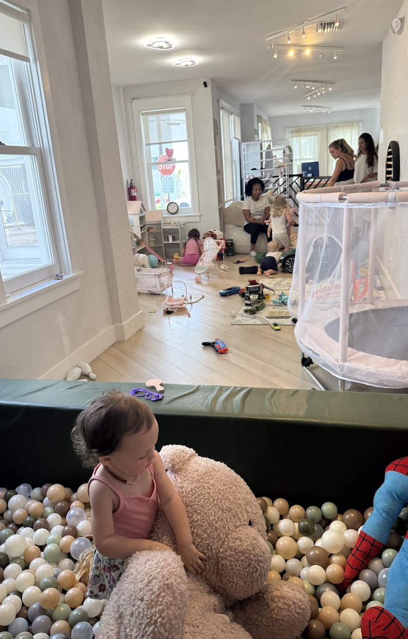 Child in the ball pit with families playing throughout the room