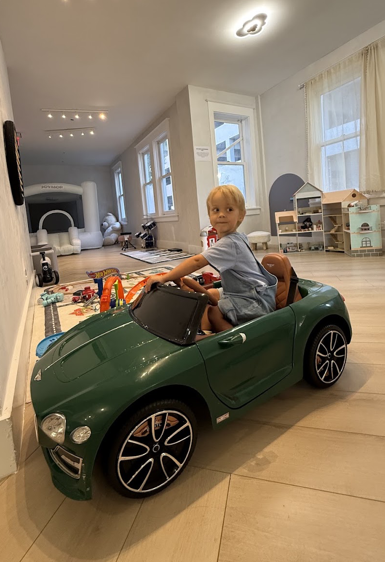 Child sitting in a green ride-on car inside the Play Area