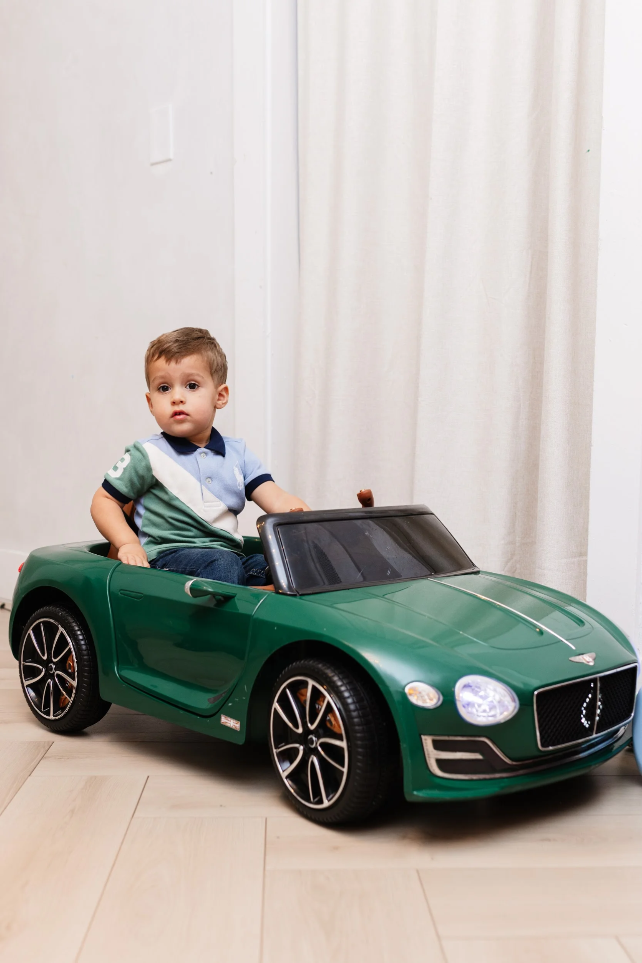 A toddler seated in a green ride-on car inside the Play Room.