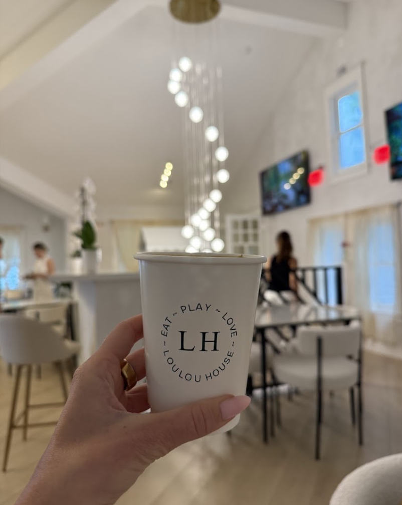 LOULOU HOUSE branded coffee cup held under the pendant lights