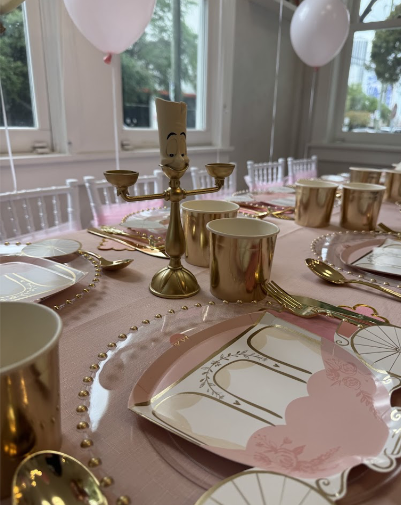 Close-up of pink and gold birthday place settings with a Beauty and the Beast candelabra