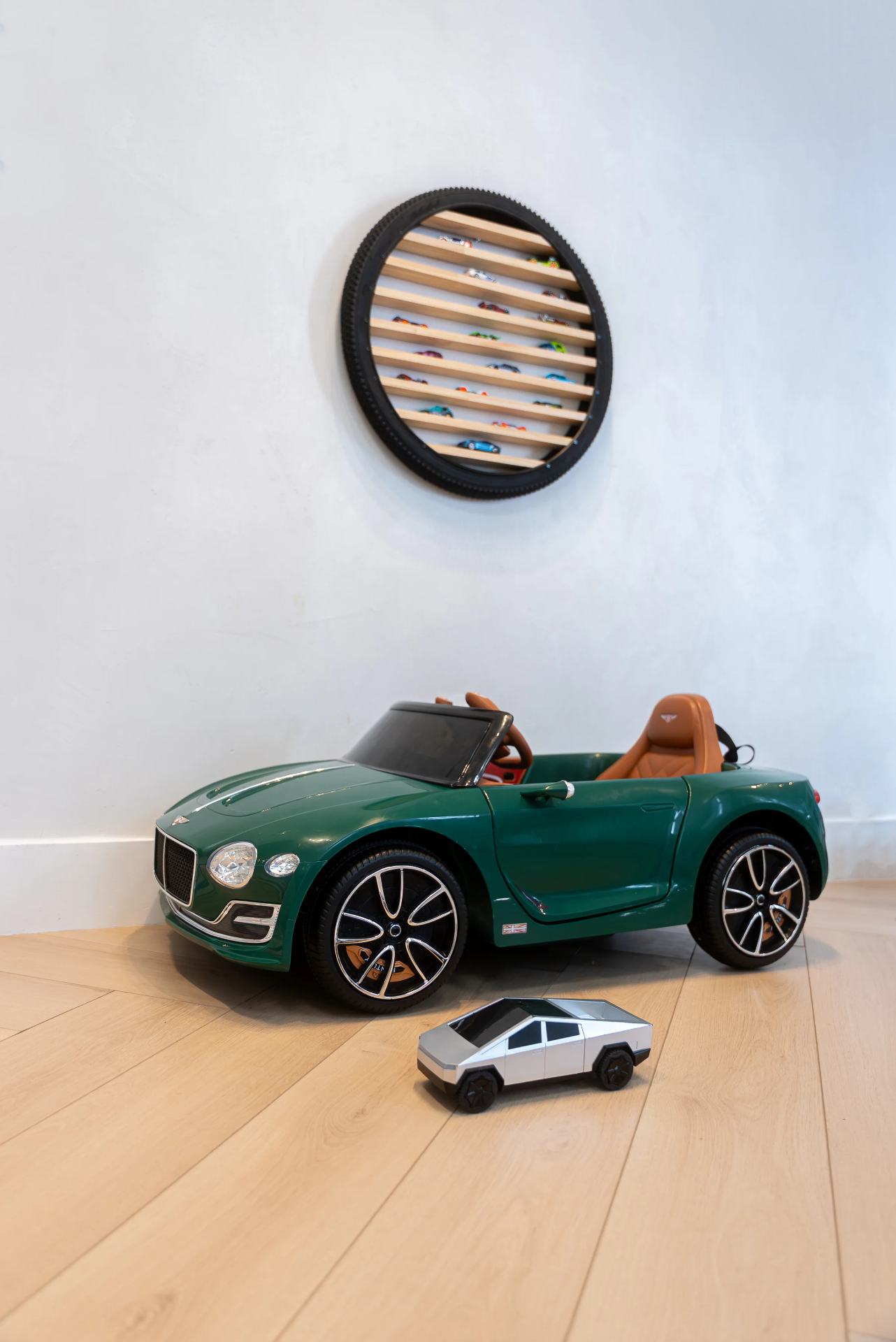 A green ride-on car beneath a circular display of miniature cars on the wall.
