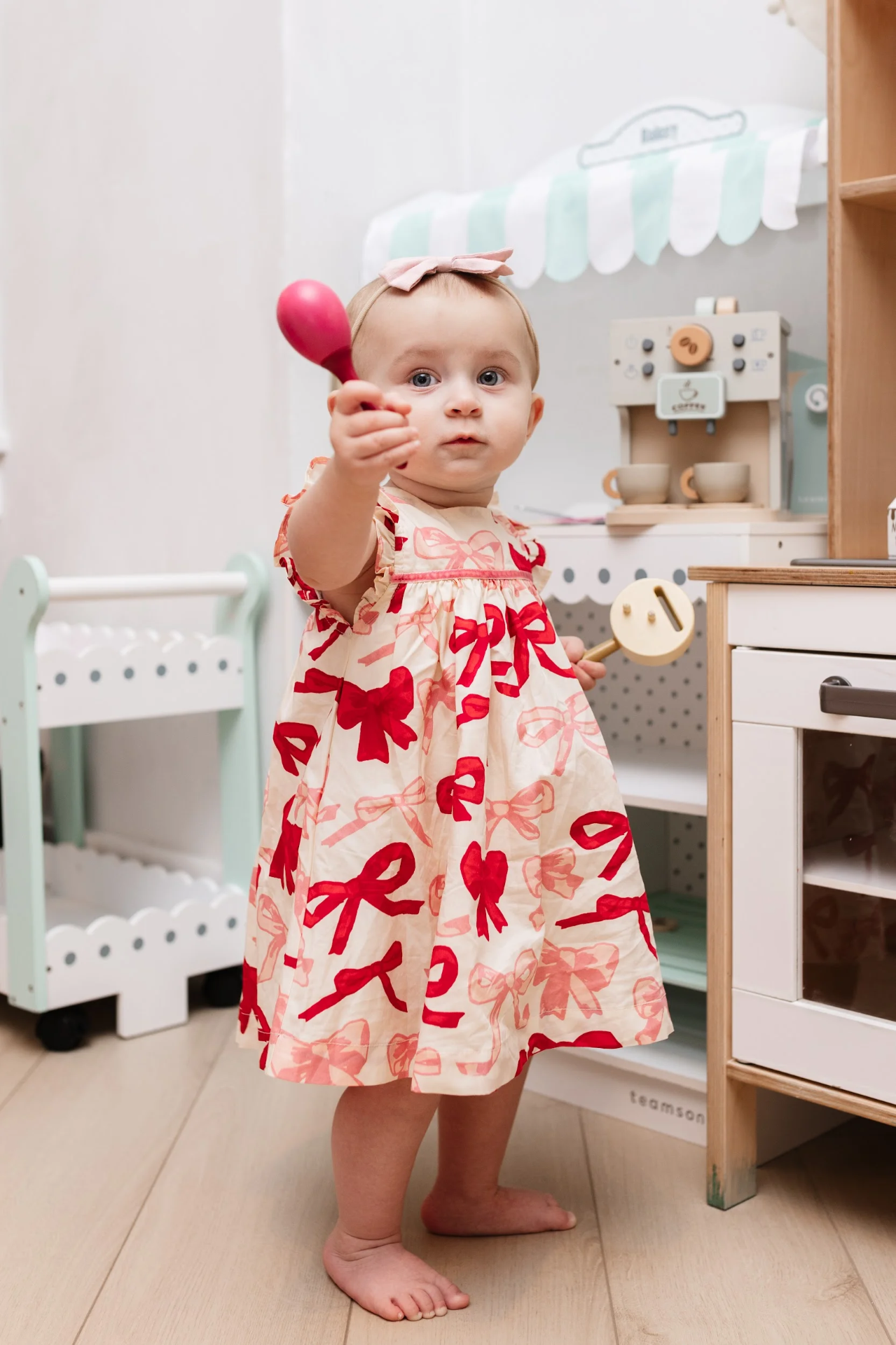 A toddler holding a toy spoon beside the pretend kitchen in the Play Room.