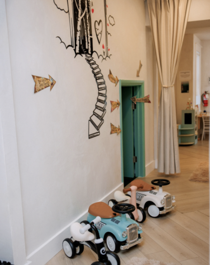 Ride-on toys lined up beneath the mural wall in the Play Area