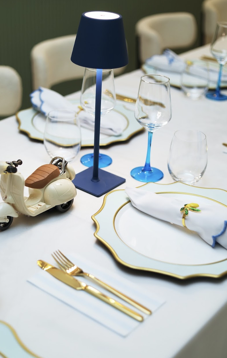 Elegant table setting with scalloped plates, blue lamp, and Vespa figurine